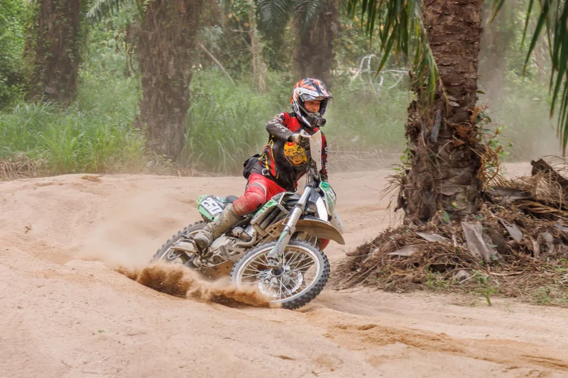 Dirt bike rider leaning into a sandy turn beside a palm