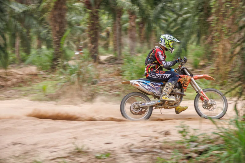 Dirt bike rider crossing a palm-lined sandy trail